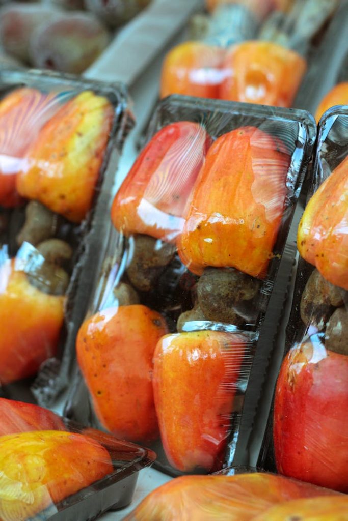Close-up of fresh cashew fruits packaged in plastic trays for sale, showcasing vibrant colors.